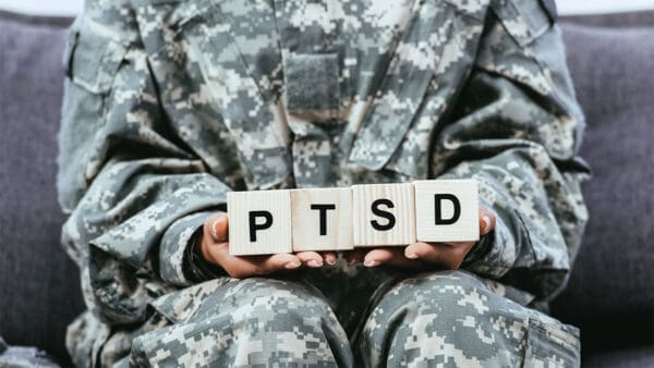 a close-up of a soldier in camo fatigues holding square blocks that spell out PTSD