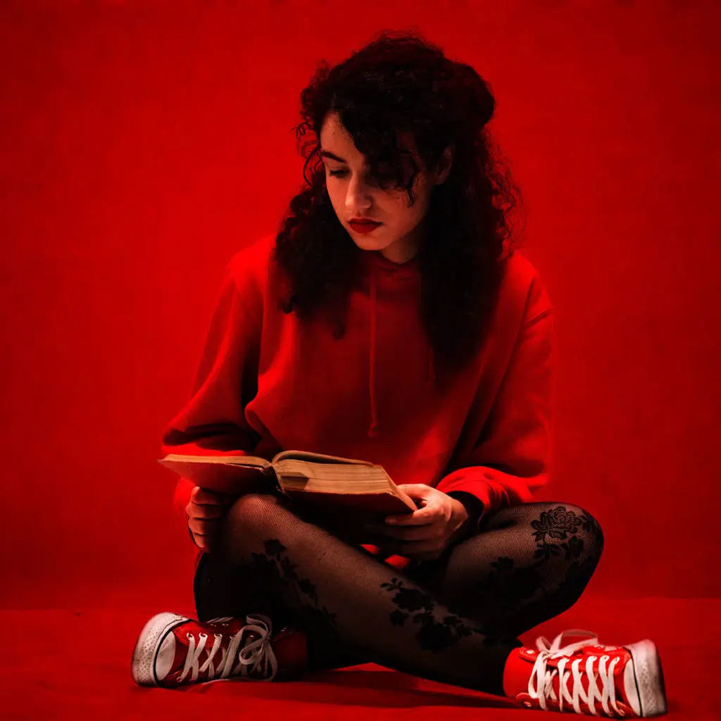 A woman in a red room sits cross legged reading a red book