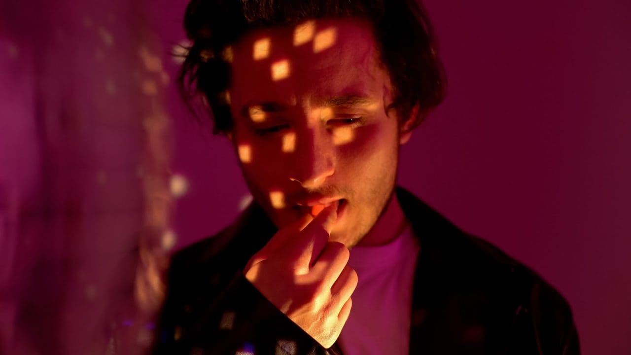 a man putting a tab of LSD into his mouth, with light reflecting onto his face