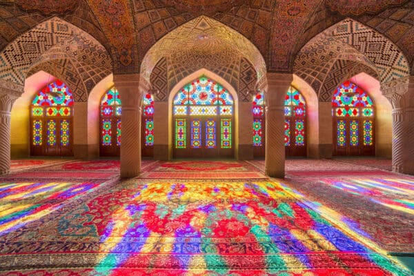 The stained-glass motifs of an Islamic mosque casts twinkling colors of kaleidoscope light onto intricately woven carpets 