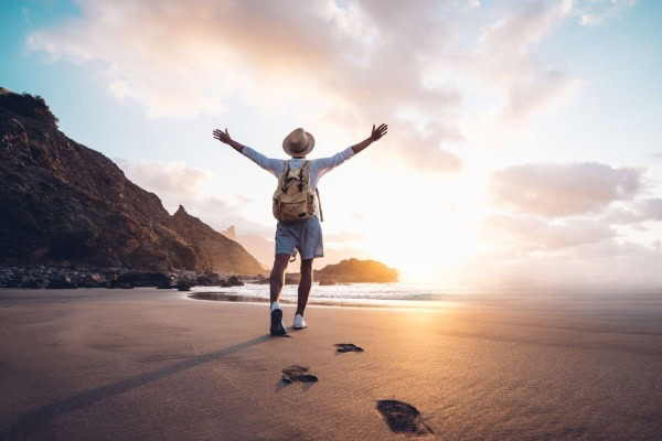 Young man arms outstretched by the sea at sunrise enjoying freedom and life, people travel wellbeing concept